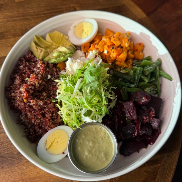 A colorful quinoa bowl with avocado, sweet potato, green beans, beets, eggs, and dressing.