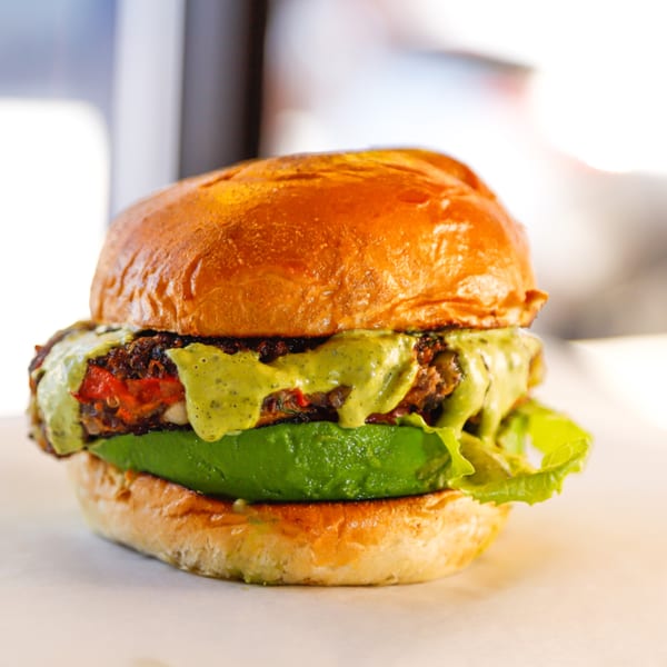 A Franks Burgers veggie burger with avocado, lettuce, and green sauce on a brioche bun.
