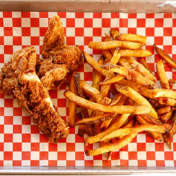 Crispy fried chicken tenders and golden french fries on red and white checkered paper.