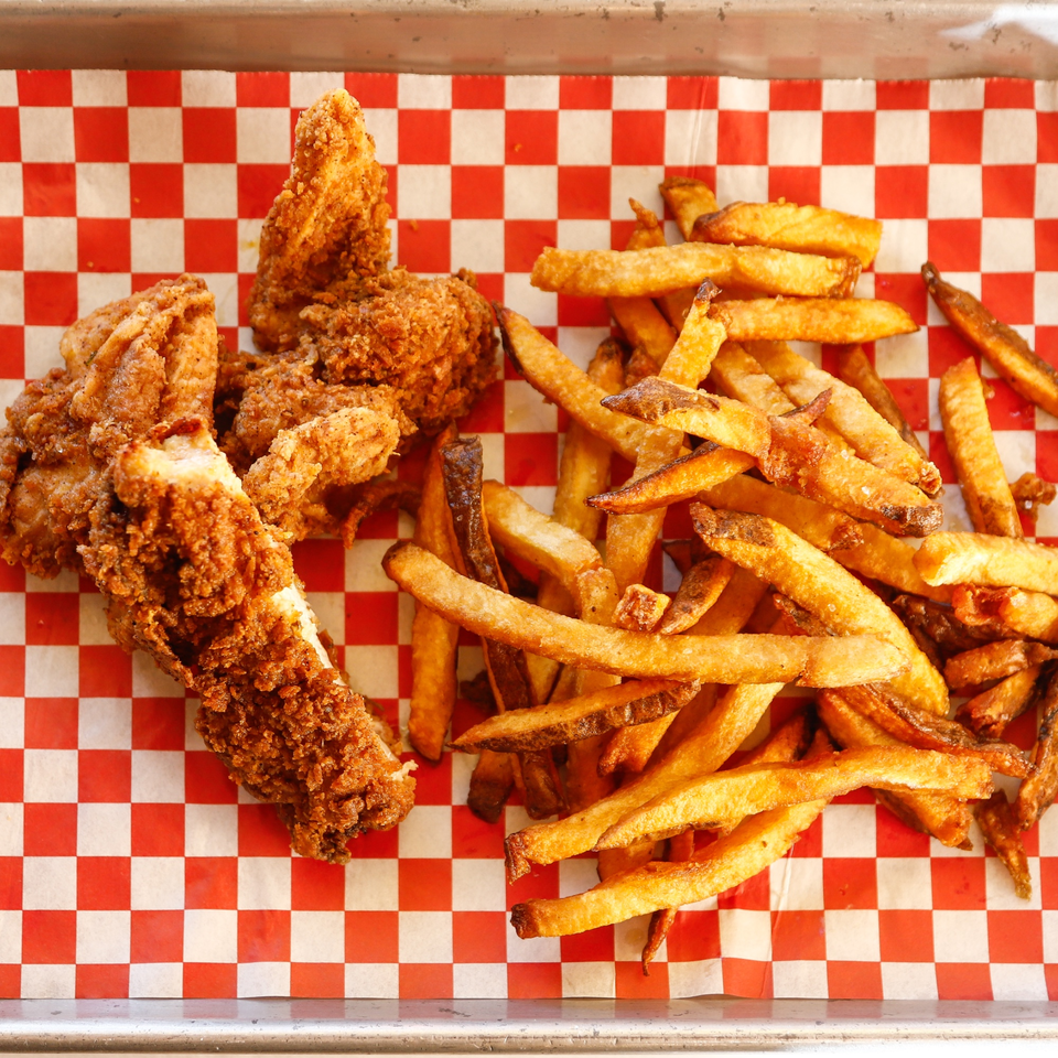 Crispy fried chicken tenders and golden french fries on red and white checkered paper.