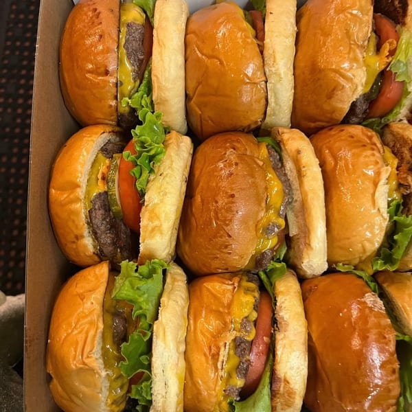 A box filled with rows of Franks Burgers sliders, featuring beef patties, cheese, lettuce, and tomatoes.