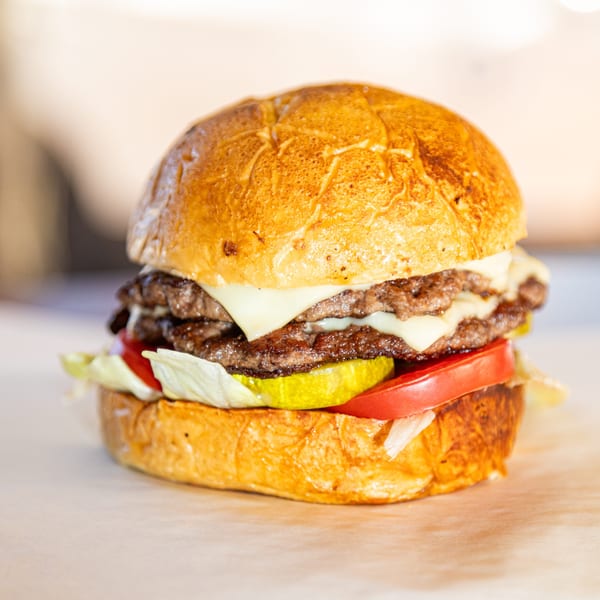 A double cheeseburger from Franks Burgers with melted cheese, lettuce, tomato, and pickles on a toasted bun.