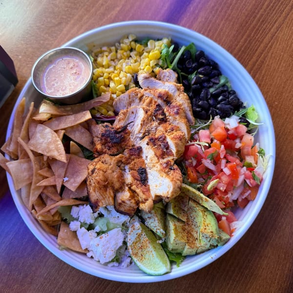 A vibrant chicken salad bowl with corn, black beans, pico de gallo, avocado, and tortilla strips.