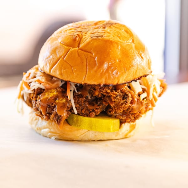 Frank's Burgers fried chicken sandwich with coleslaw, pickles, and sauce on a brioche bun.