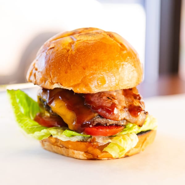 A Franks Burgers cheeseburger with bacon, lettuce, tomato, and BBQ sauce on a brioche bun.