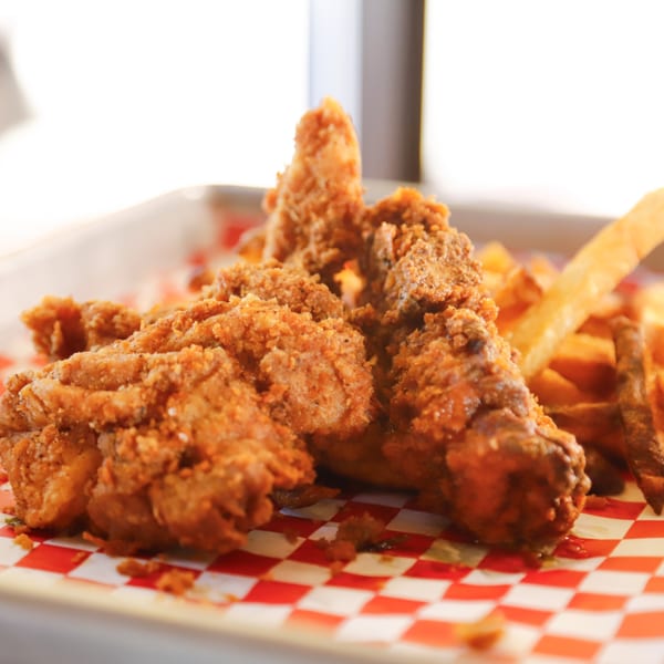 Crispy fried chicken tenders and golden french fries on red and white checkered paper.