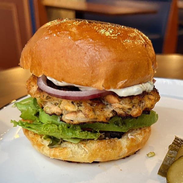 A Franks Burgers salmon burger with lettuce, red onion, and white sauce on a brioche bun.